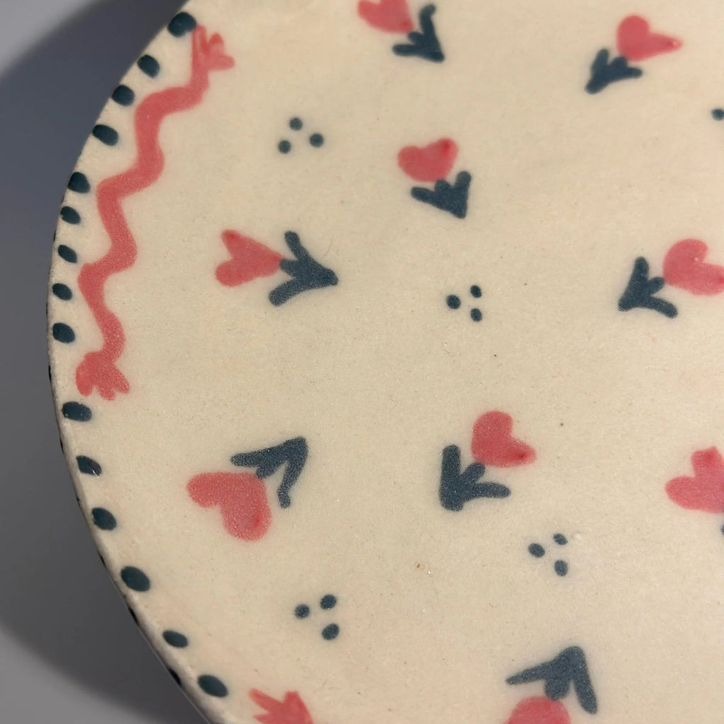 Close-up of a ceramic floral hearts plate with pink and green  decorative patterns